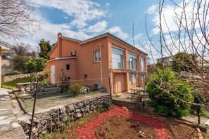 Ein zweistöckiges Haus mit einer Steinmauer, einem Garten mit roter Mulchschicht und einem strahlend blauen Himmel.