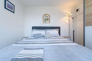Ein ordentlich bezogenes Bett mit einer Streifenoptik-Decke, einem Kopfteil und einem gerahmten Bild an der Wand.
