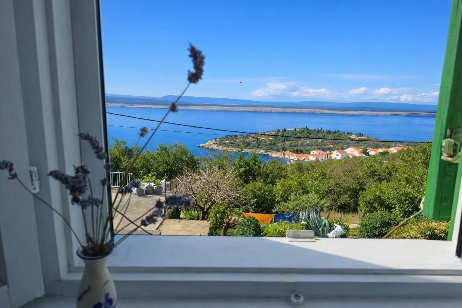 A view from a window overlooking a coastal area with a clear sky, a distant island, and a green building.