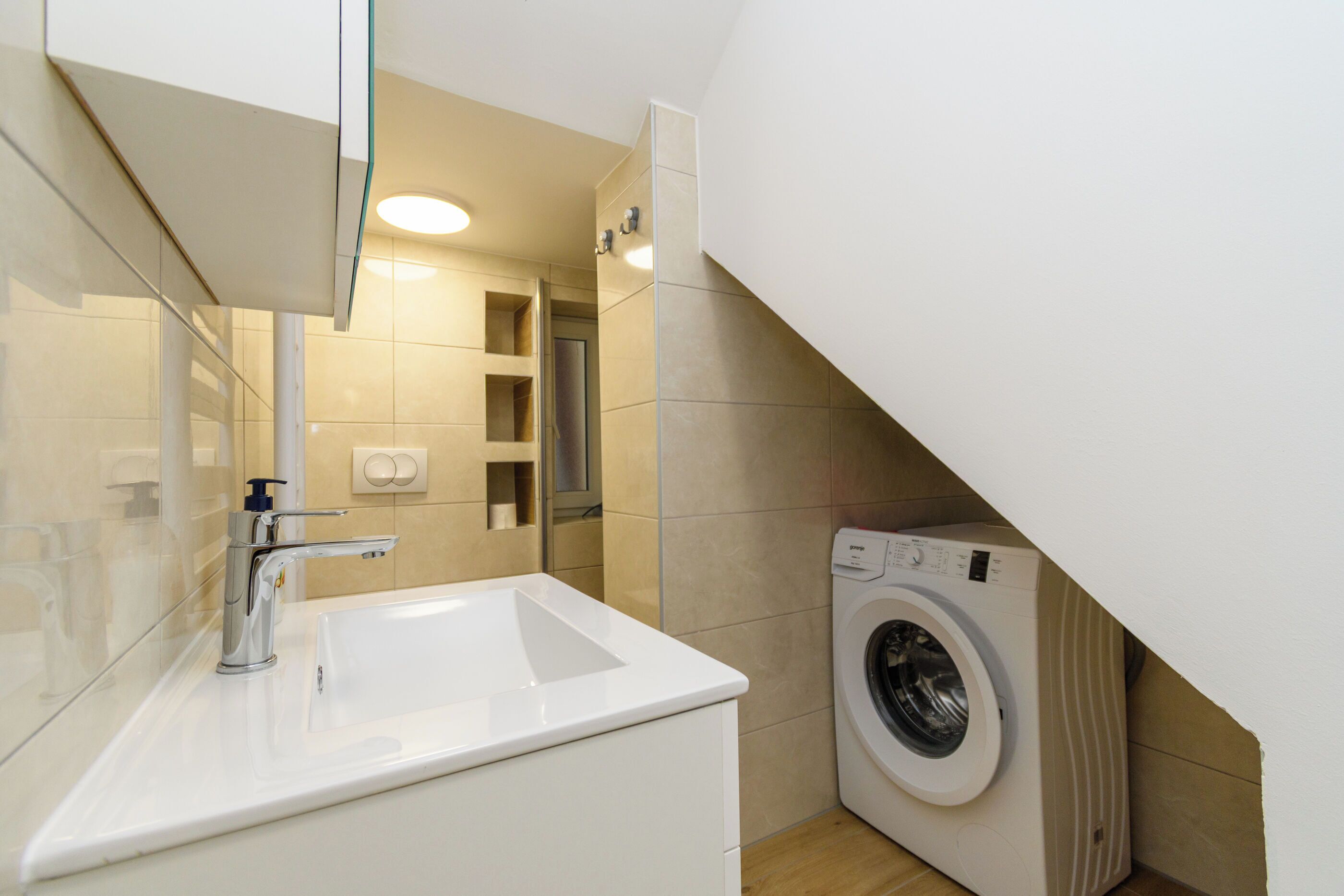 A modern bathroom with a sink, mirror, and washing machine.