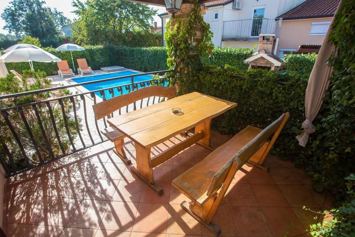 Ein Holztisch und eine Bank auf einem Balkon mit einem Pool im Hintergrund.