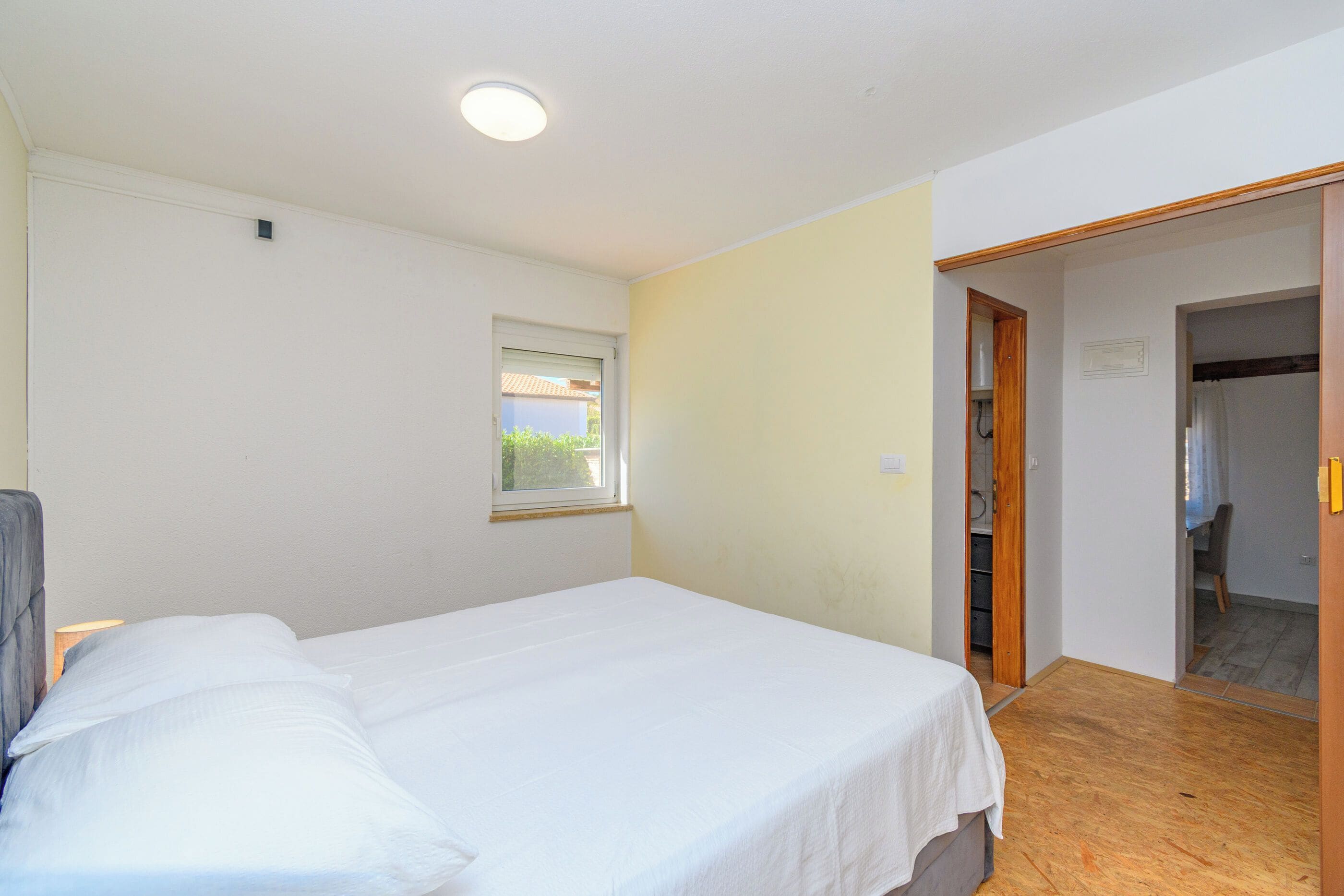 Een slaapkamer met een bed, een raam en een deur naar een badkamer.
