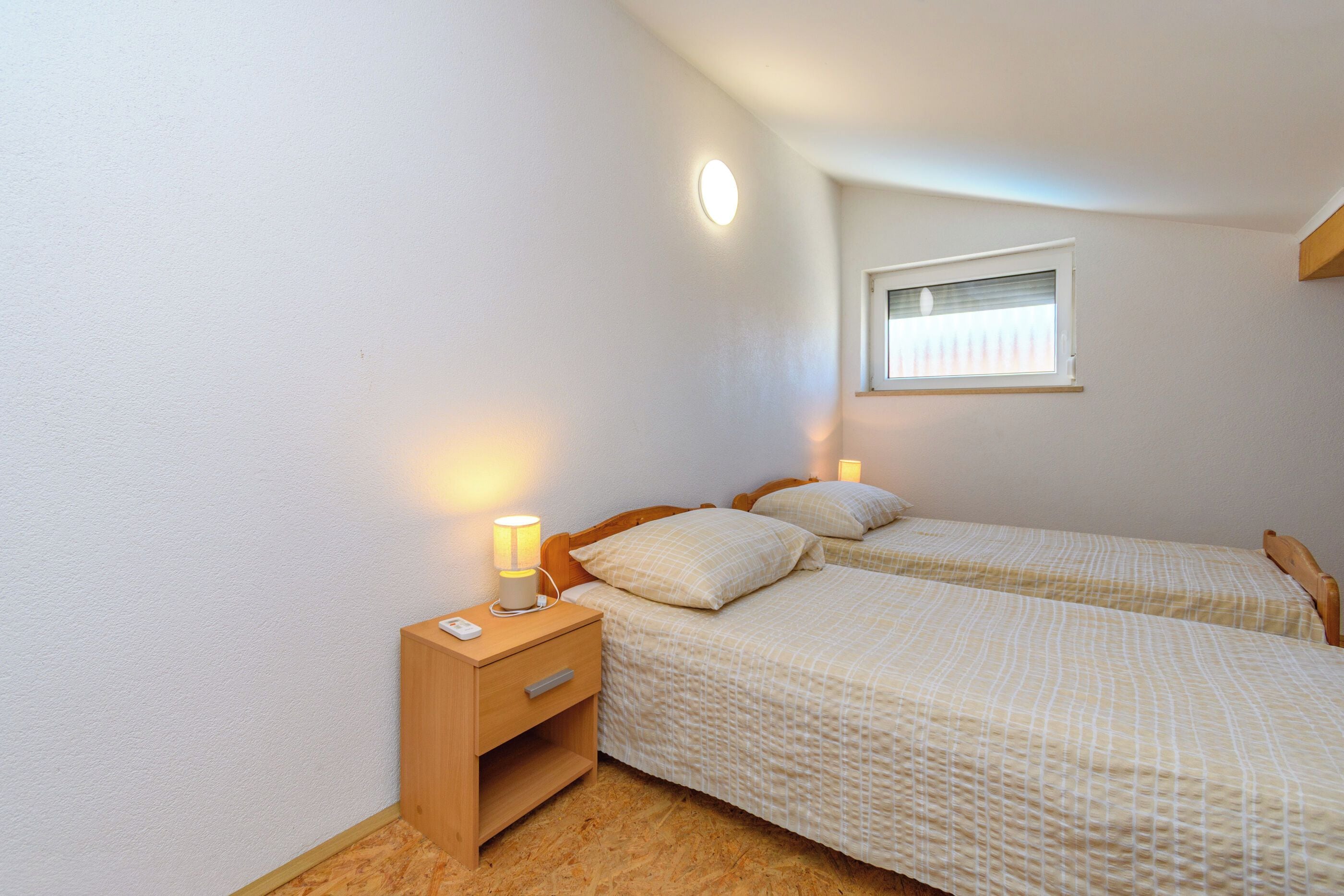 Une chambre avec deux lits, une table de chevet, une lampe de chevet, une fenêtre et un luminaire fixé au mur.