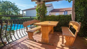 Ein Holztisch und -bänke auf einer Terrasse, im Hintergrund ein Schwimmbad.