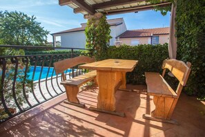 Ein Holztisch und -bänke auf einer Terrasse, im Hintergrund ein Schwimmbad.