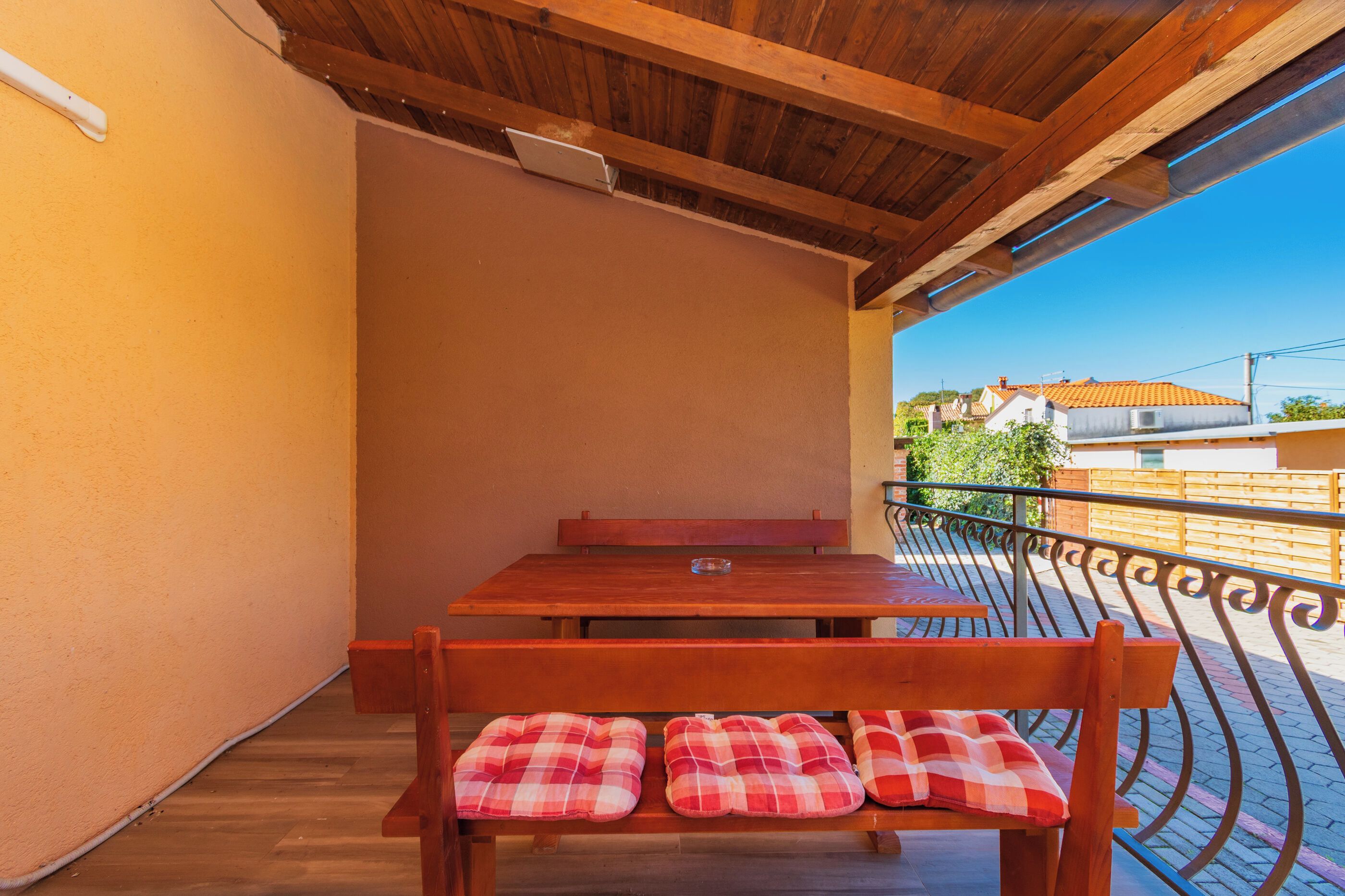 Una mesa y banco de madera con cojines de cuadros en un balcón con vistas a edificios.