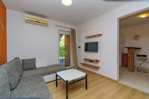 A living room with a grey sofa, a white coffee table, a flat-screen TV mounted on the wall, and a sliding glass door leading to an outdoor area. - Apartments Eny (Porec)
