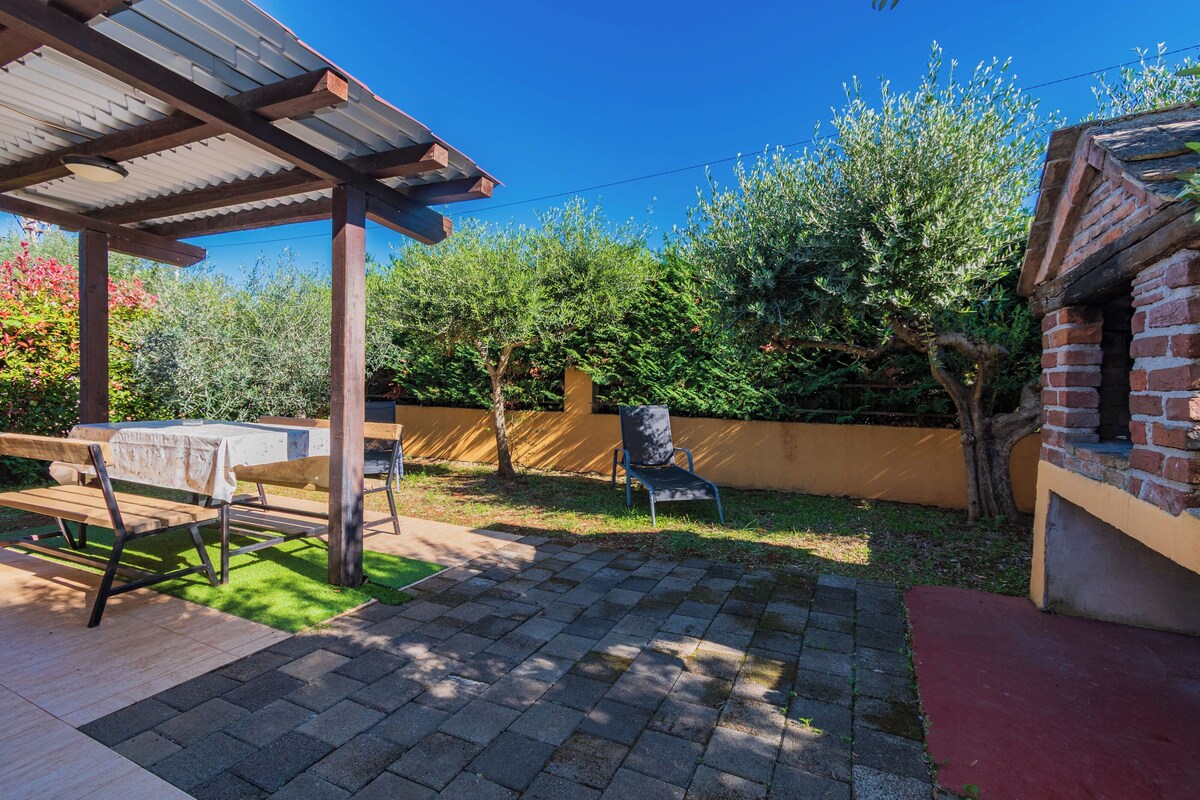 A patio area with a pergola, a table with benches, and a brick structure.