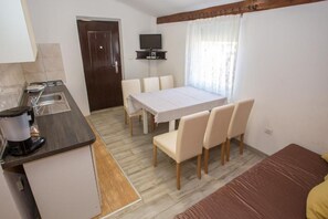 A compact room with a kitchenette, a dining table with chairs, a bed, and a television mounted on the wall. - Apartments Eny (Porec)