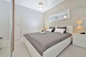 A modern bedroom with a large bed, bedside lamps, a mirror, and a door. - Apartments Sundream (Sukosan)