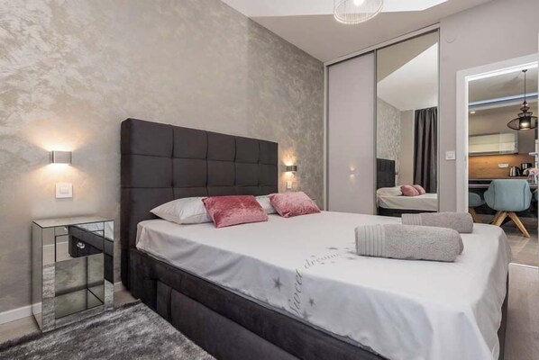A modern bedroom with a large bed, bedside tables, a mirror, and a view into the adjacent bathroom. - Apartments Sundream (Sukosan)