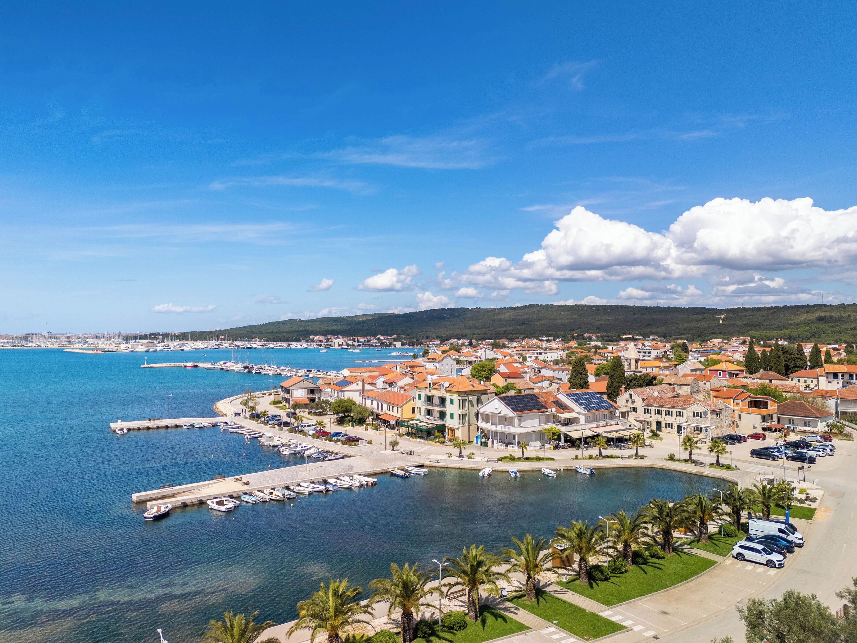 A coastal town with a marina, buildings with red roofs, and a clear blue sky.