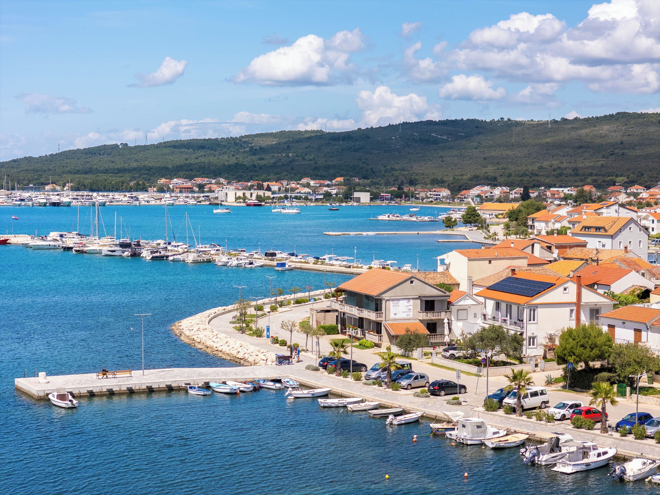 A coastal marina with boats, a pier, and residential buildings with red-tiled roofs.