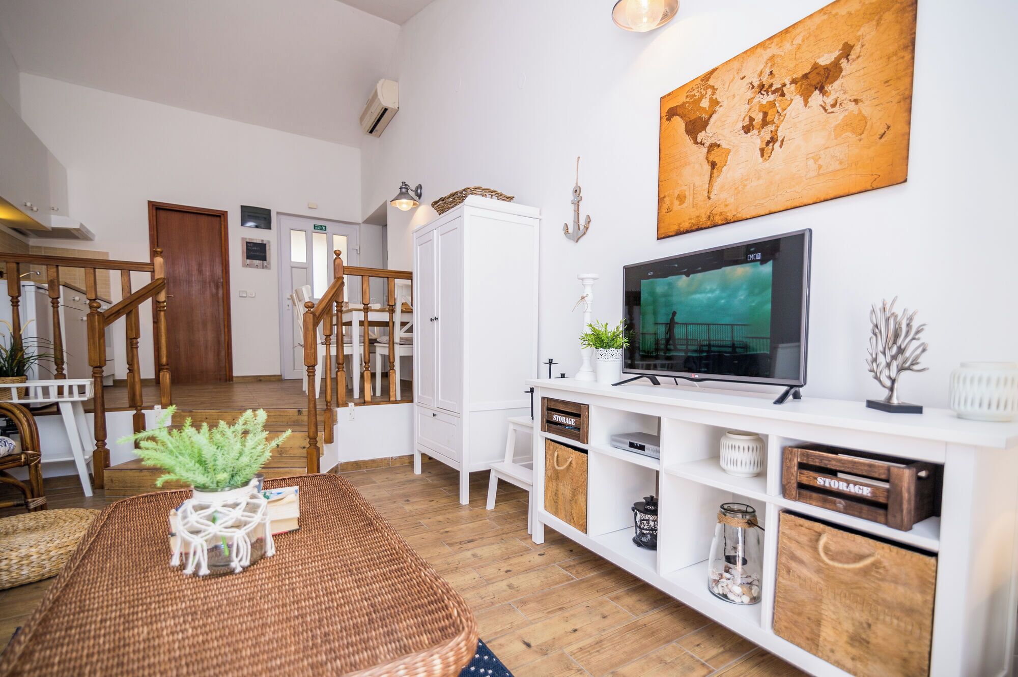 A modern living room with a TV, storage units, a staircase, and a dining area.