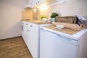 A kitchen with white cabinets, a wooden countertop, a washing machine, and a wicker basket with towels. - Apartments Tellus (Biograd na Moru)