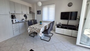 Une cuisine moderne avec des meubles blancs, une table à manger avec des chaises, un téléviseur et une horloge au mur.