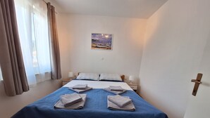 Une chambre à coucher avec un lit, deux tables de chevet, une commode, un tableau accroché au mur et une porte dotée d’une poignée.