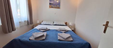 A bedroom with a bed, two bedside tables, a nightstand, a painting on the wall, and a door with a handle.