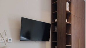 Un salon moderne avec un téléviseur à écran plat fixé au mur, une bibliothèque en bois, un banc avec un livre et une petite table avec une lampe.