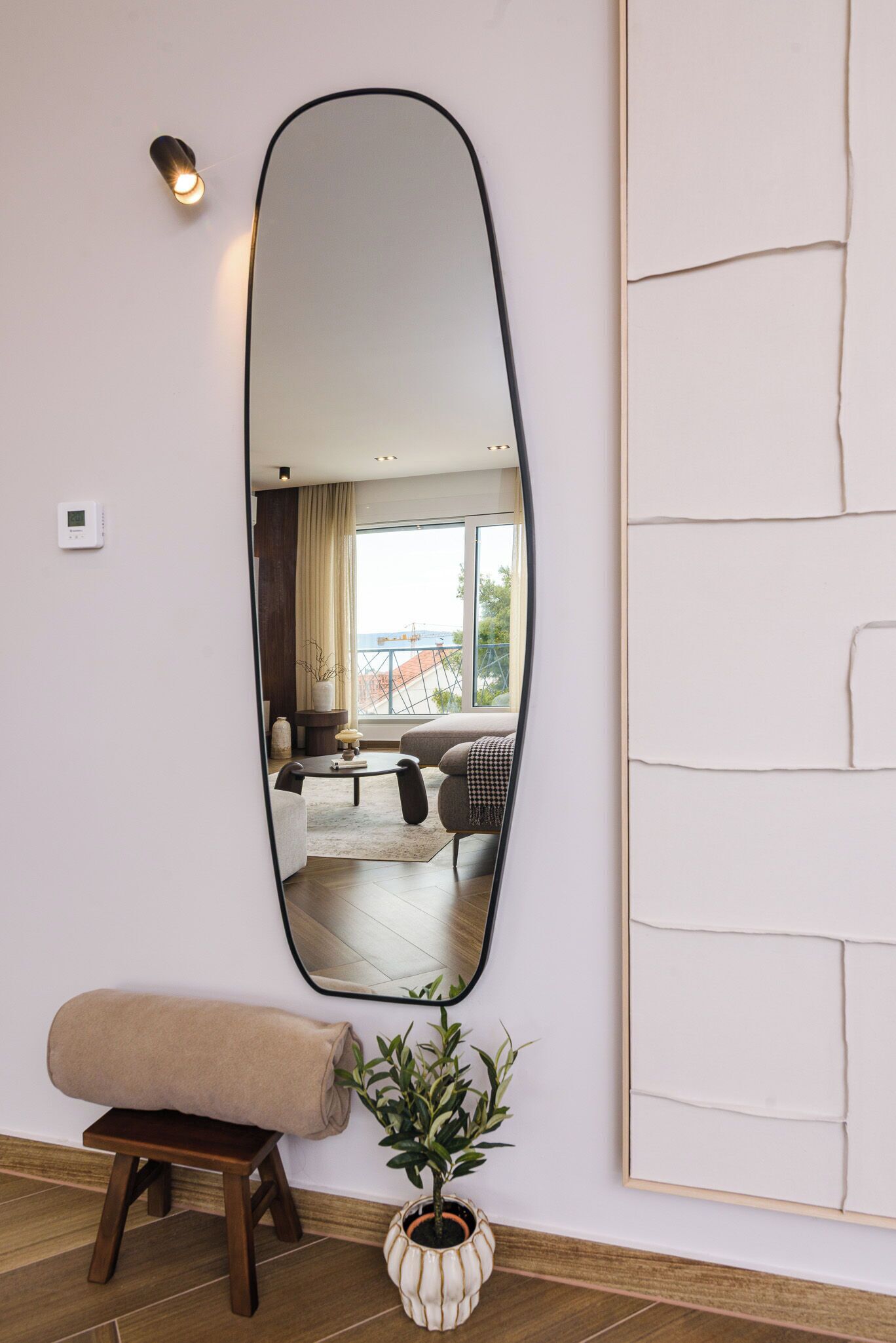A room with a large mirror, a bench, a potted plant, and a framed artwork on the wall.
