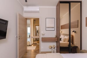 Un dormitorio moderno con una cama, un televisor, una puerta de madera y un pasillo que conduce a otra habitación.