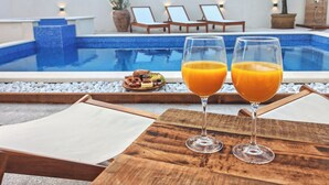 Une scène au bord de la piscine avec deux verres de jus d’orange, une table en bois et des chaises longues.