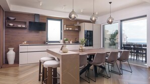 Une cuisine moderne dotée d’un îlot central, de tabourets de bar, de luminaires suspendus et d’une grande fenêtre offrant une vue dégagée.