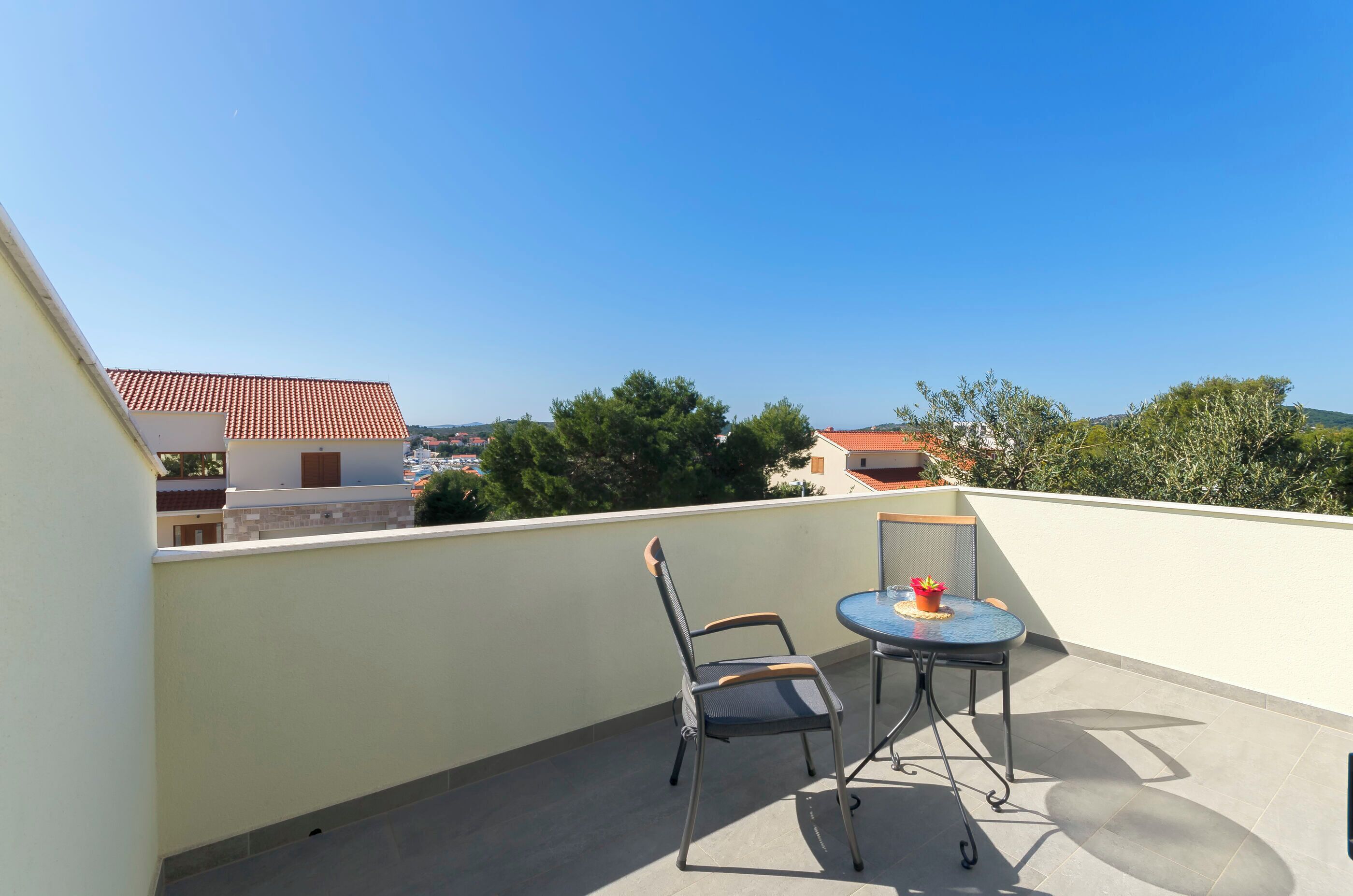 A balcony with a table and chairs, a clear view of buildings and trees, and a tiled floor.