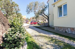 A residential street with parked cars, a building with a stone base, and a tree with white flowers.