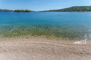 A clear view of a pebble beach leading to a calm sea with a distant island and hills.