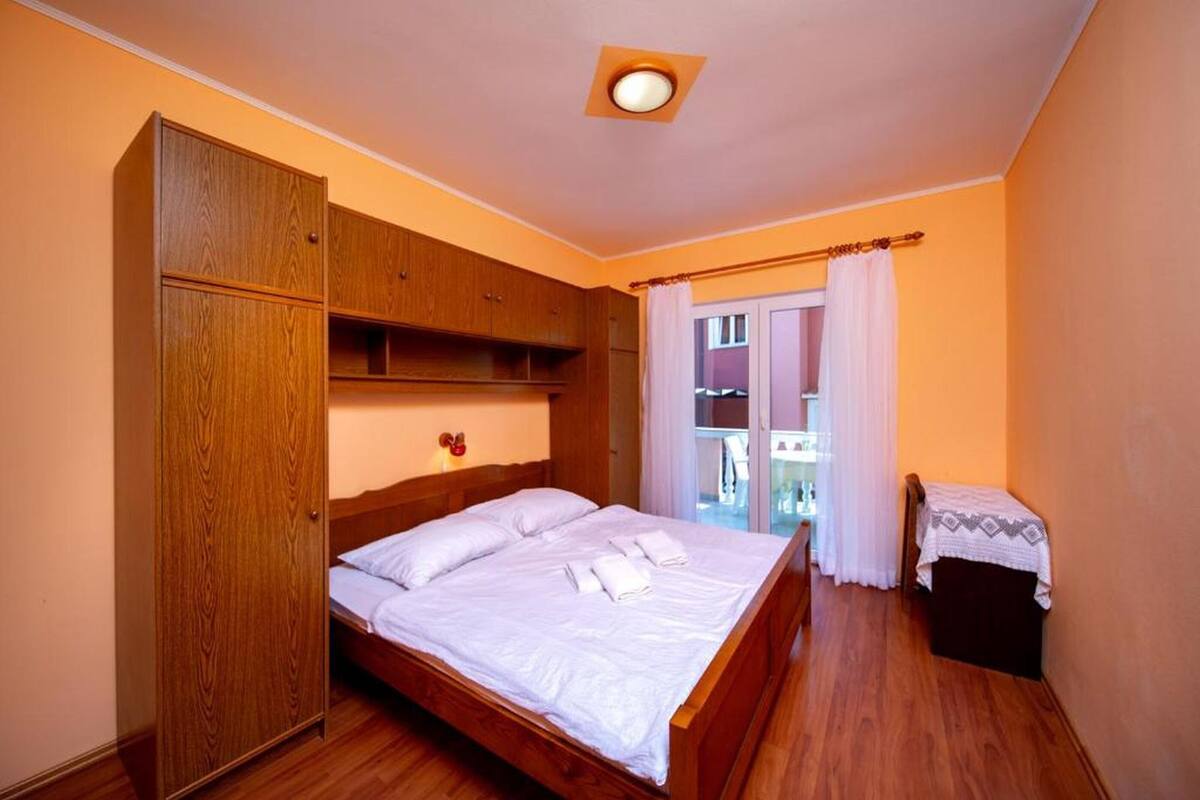 A bedroom with a wooden bed, a wardrobe, a small table, and a view through a window.