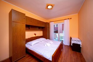 A bedroom with a wooden bed, a wardrobe, a small table, and a view through a window.