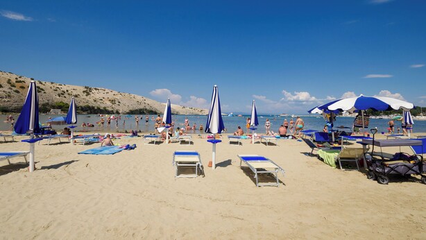 Een strand met ligbedden en parasols, een heldere lucht en een rustige zee.