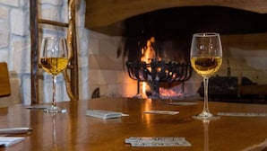 Een tafel met twee glazen witte wijn en speelkaarten, voor een stenen muur en een open haard.