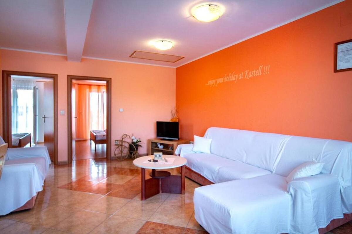 A hotel room with a white sofa, a TV on a stand, a small table, and a wall with a message.