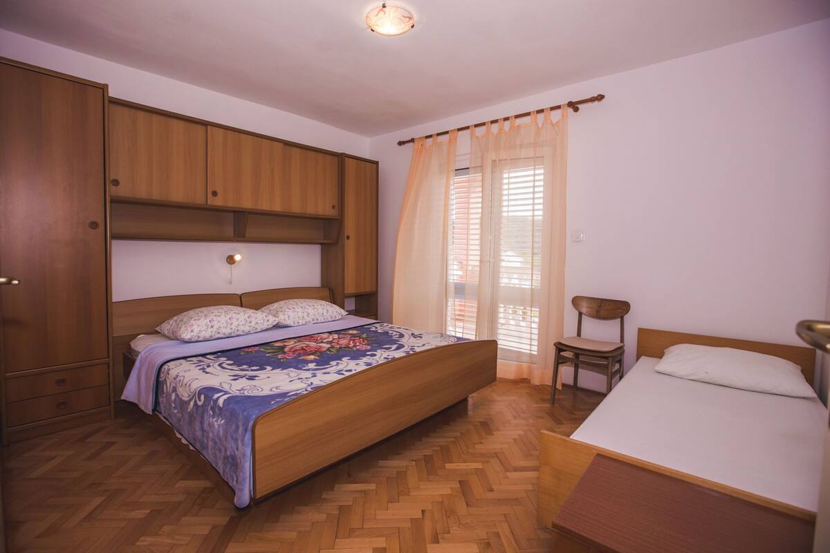 A bedroom with a wooden bed, a smaller bed, a wardrobe, and a chair.