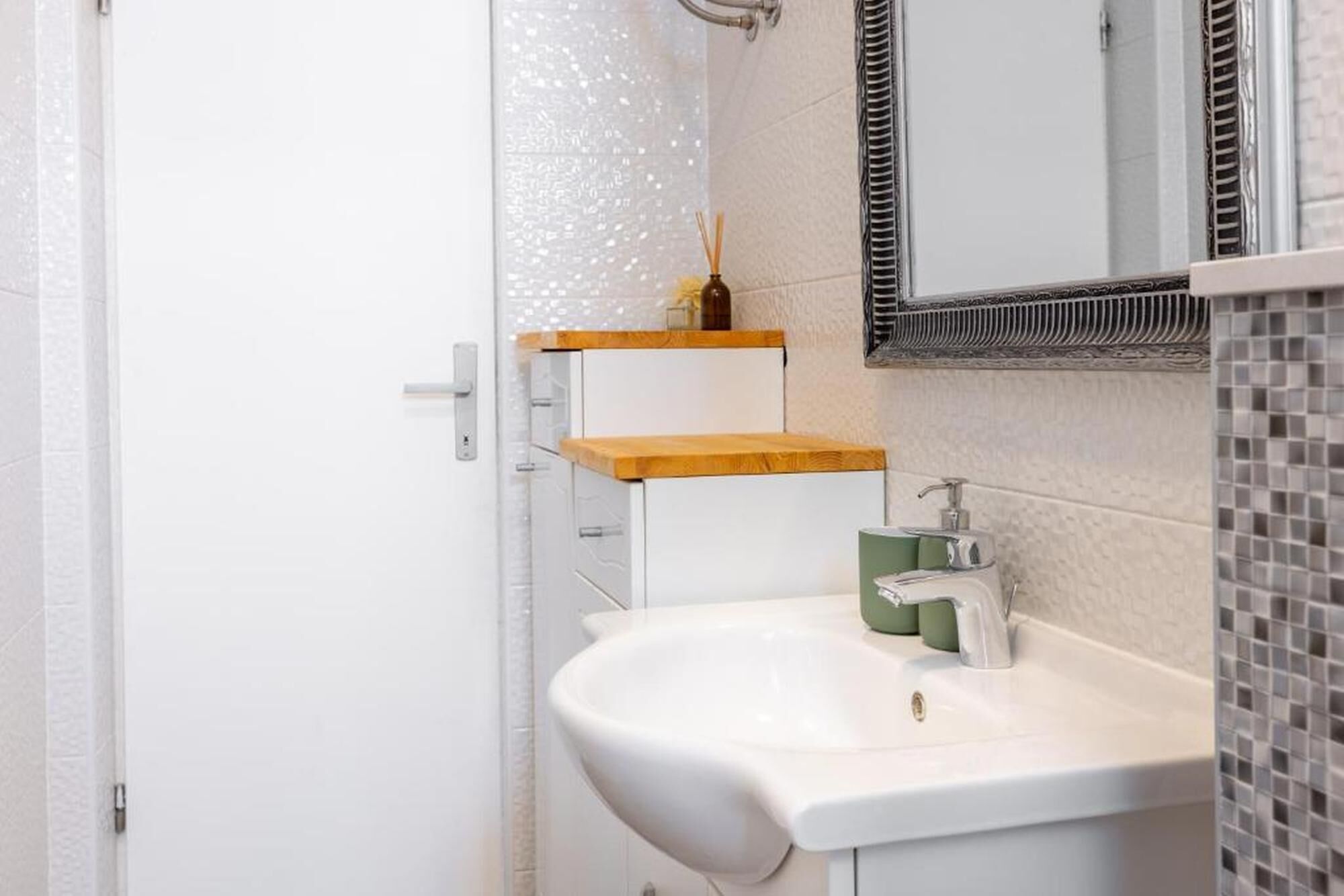 Een badkamer met een wit wastafelmeubel, een spiegel en een douchehoek.