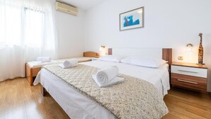 Et hotelværelse med to senge, et stort vindue med gardiner, en aircondition, et billede i ramme på væggen, og et natbord med lampe og en giraf-figur.