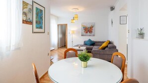 En moderne stue med sofa, spisebord og et køkken i baggrunden.