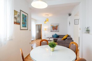 A modern living room with a sofa, a dining table, and a kitchen in the background. - Apartments Azure View (Makarska)