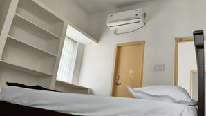 A single bed with white bedding, a wooden headboard, a wall-mounted air conditioner, a door with a handle, and a window with blinds. - Cozy & Comfortable Serviced Apartment in AS Rao Nagar,ECIL, Secunderabad (Secunderabad)
