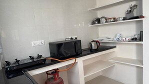 A kitchen with a gas stove, a microwave, a kettle, and a gas cylinder. - Cozy & Comfortable Serviced Apartment in AS Rao Nagar,ECIL, Secunderabad (Secunderabad)