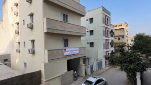 A multi-story residential building with a service entrance, a parked car, and a small trash bin. - Cozy & Comfortable Serviced Apartment in AS Rao Nagar,ECIL, Secunderabad (Secunderabad)