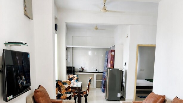 A living room with sofas, a coffee table, a TV, and a kitchen in the background. - Cozy & Comfortable Serviced Apartment in AS Rao Nagar,ECIL, Secunderabad (Secunderabad)