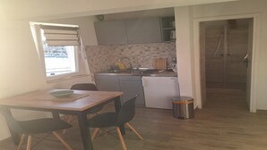 A compact kitchen with a dining area, a window with blinds, and a shower room. - Apartments Ivan (Tisno)