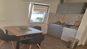 A compact kitchen with a dining area, a window with a view, and a trash bin. - Apartments Ivan (Tisno)