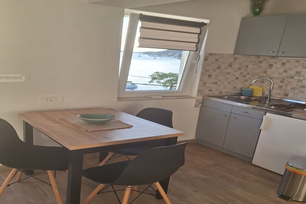 A compact kitchen with a dining area, a window with a view, and a trash bin.