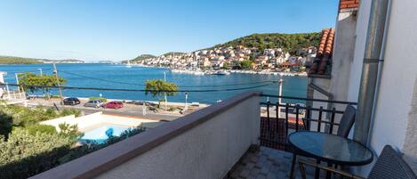 Uma varanda com vista para uma cidade costeira, uma piscina e uma mesa com cadeiras.