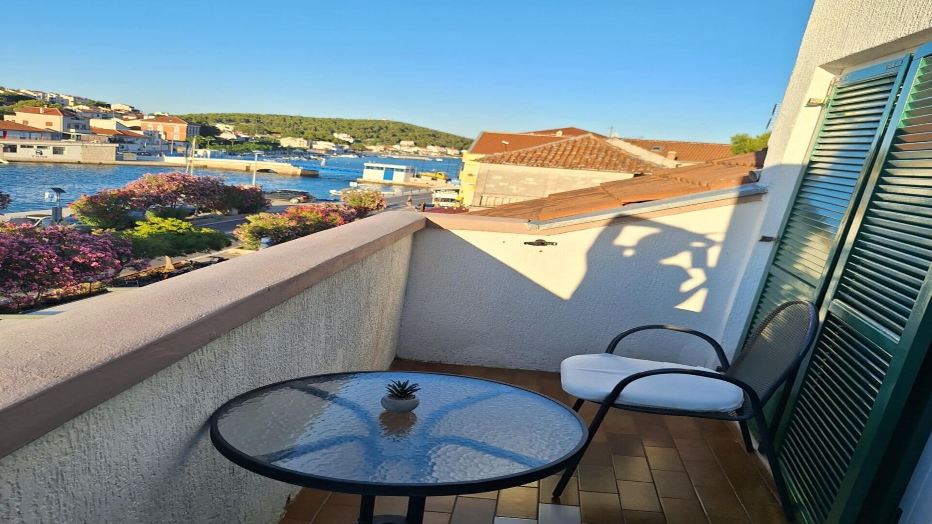 Un balcón con mesa y sillas, con vistas a un pueblo costero con edificios y un puente.