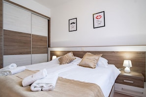 A hotel room with a large bed, two pillows, a nightstand with a lamp, and two framed pictures on the wall. - Apartments Mistral (Lopar)